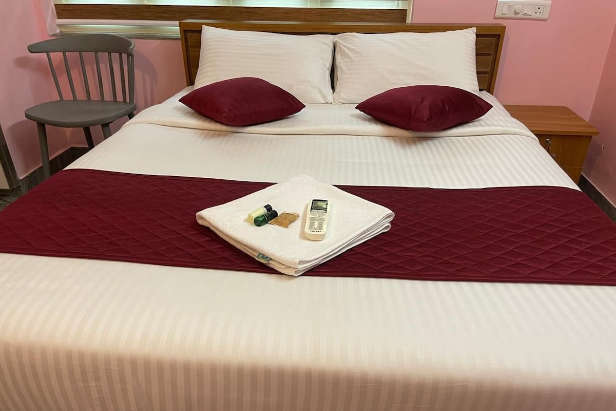 A neatly made bed with a red blanket, pillows, and a folded towel with toiletries.