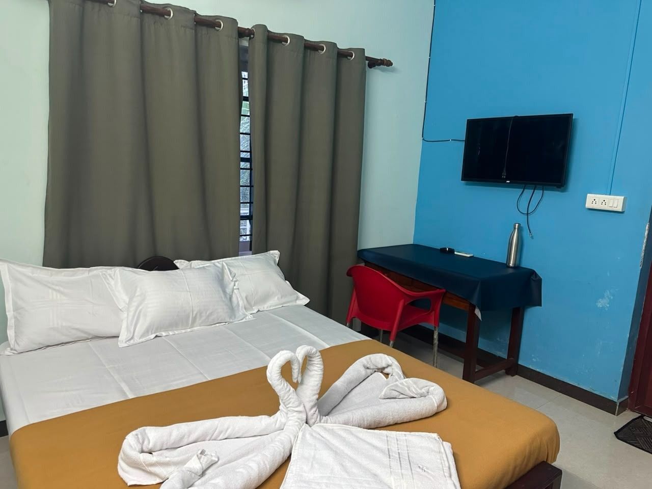 Quarto de hotel com cama, secretária, televisão e janela com cortinas.