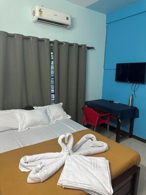 Habitación de hotel con cama, escritorio, televisión y ventana con cortinas.