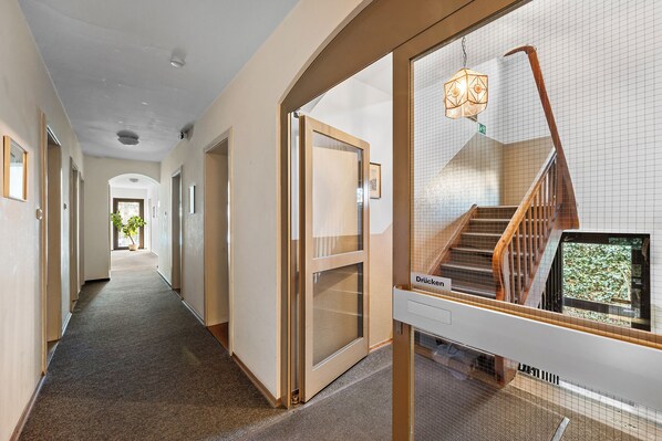 Pasillo de hotel con vista a una escalera y una puerta con la leyenda 'Drucken'.