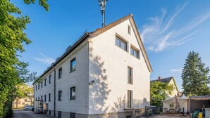 Un edificio de dos pisos con techo plano, balcón y un pequeño espacio al aire libre para sentarse.