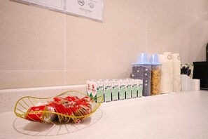 A kitchen counter with a basket of biscuits, stacks of milk cartons, and a row of disposable cups.