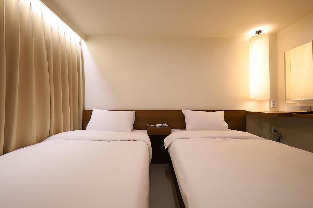 Ein Hotelzimmer mit zwei Betten, einem Nachttisch, einer Lampe und einem Spiegel.