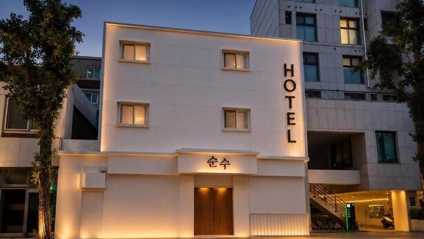 Un moderno edificio de hotel con un llamativo letrero que dice 'HOTEL', un acceso cubierto y una escalera que conduce a un nivel superior.
