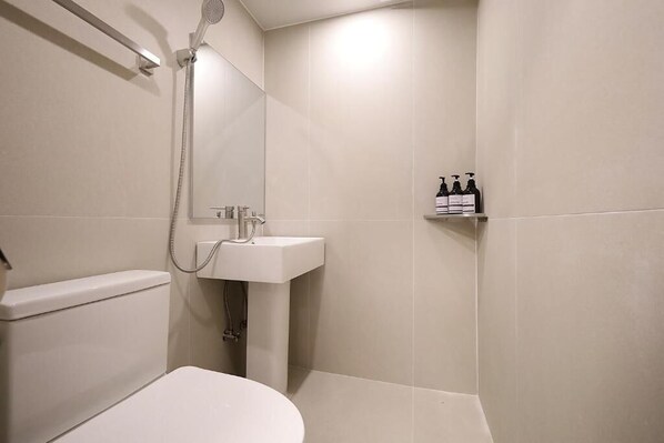 A bathroom with a toilet, a sink, a shower, and a shelf with toiletries. - Sunsu Hotel Mia (Seoul)
