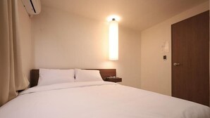 Habitación de hotel con una cama individual, una mesita de noche, una lámpara de pared y una puerta.