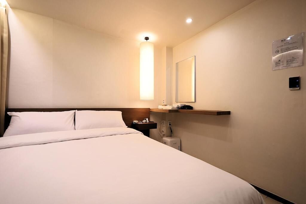 Une chambre d’hôtel avec un lit, une table de chevet, une lampe et un miroir au mur.