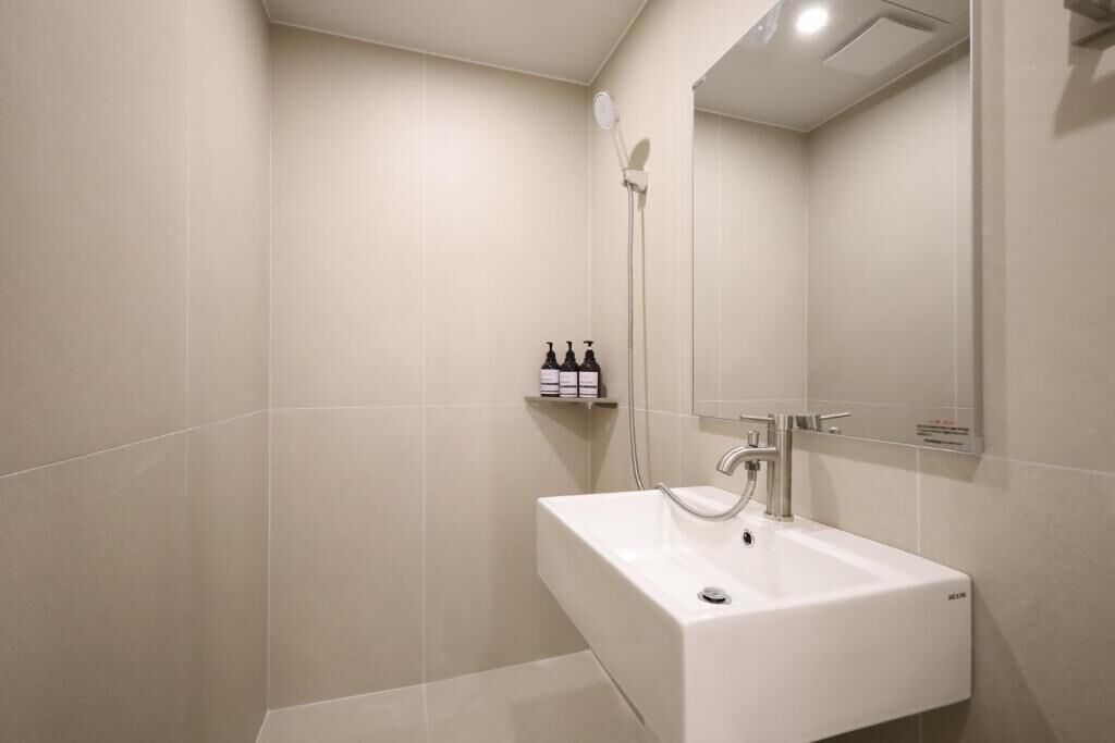 A modern bathroom with a white sink, a handheld showerhead, and a shelf with toiletries.