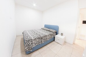 A bedroom with a zebra-patterned bedspread, a blue headboard, and a white bedside table with drawers. - Huge Terrace Sea Front (Bosa Marina)