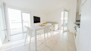A bright, modern kitchen with white cabinetry, a dining table with chairs, and a TV mounted on the wall. - Huge Terrace Sea Front (Bosa Marina)