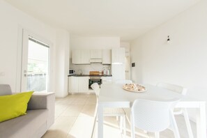 A modern kitchen with white cabinets, a dining table with chairs, and a sofa with a green pillow. - Huge Terrace Sea Front (Bosa Marina)