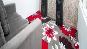 Ett rum med en grå soffa, en platt-TV som är monterad på väggen och två höga högtalare.