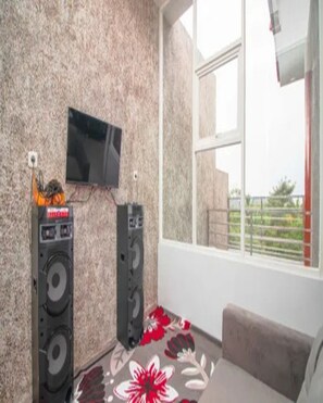 A room with a television mounted on the wall, two speakers, a window with a view, and a floral carpet. - Cozzy Villa Evergreen (batu)