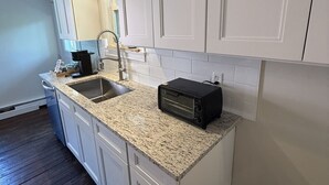 Cocina con armarios blancos, encimera de granito, tostadora y un lavabo.