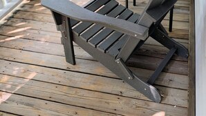 Terraza de madera con sillas Adirondack y una cerca blanca.