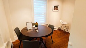 Un comedor con una mesa redonda, cuatro sillas, una planta en maceta y un cuadro en la pared.