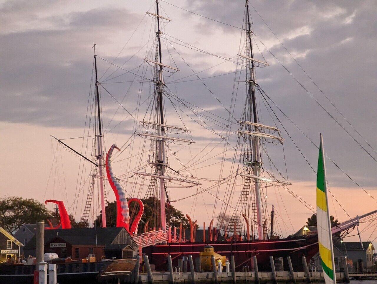 A large sailing ship docked at a harbor with a dock office nearby.