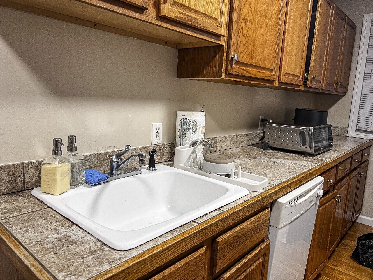 A kitchen with a double sink, wooden cabinets, a microwave, and a dishwasher.