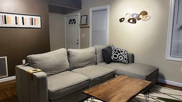 A living room with a grey sectional sofa, a wooden coffee table, and a patterned rug.
