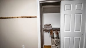 A room with a wooden floor, a white door, and a closet with hanging clothes and a folded towel. - Quiet 1st-Floor 2BR Haven w/ King Bed, Desks, In-Unit Laundry & 2-Car Parking | Walk to Yale (New Haven)