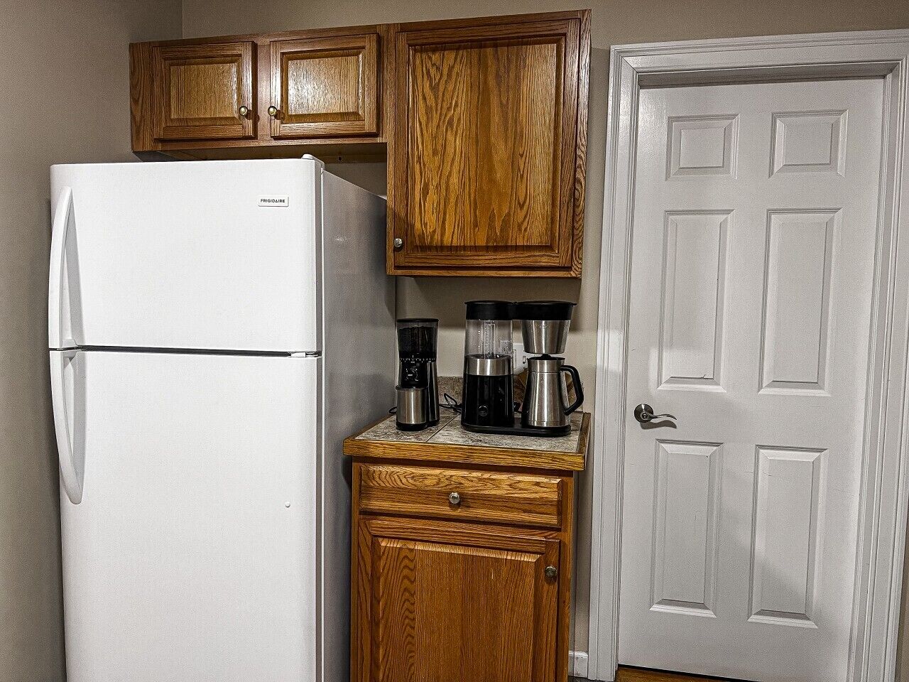 A compact kitchen with a white refrigerator, wooden cabinets, a coffee maker, and a door.