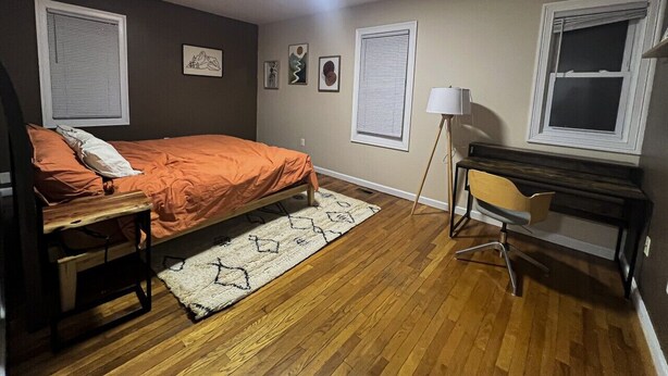 A bedroom with a bed, a desk, and a chair. There are two windows with blinds, a lamp, and a rug on the floor. - Quiet 1st-Floor 2BR Haven w/ King Bed, Desks, In-Unit Laundry & 2-Car Parking | Walk to Yale (New Haven)