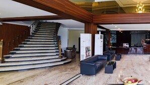 Vestíbulo de hotel con una escalera monumental, una recepción y una zona de estar.