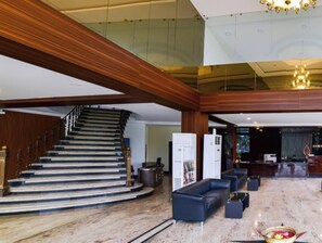 A hotel lobby with a grand staircase, a reception desk, and a seating area.