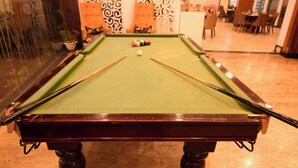 Una mesa de billar con bolas y tacos, rodeada de sillas y un pared con diseño.