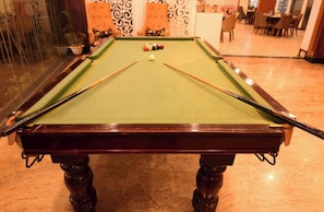 A pool table with balls and cues, surrounded by chairs and a patterned wall.
