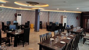 Un restaurante con varias mesas y sillas, papel tapiz estampado e iluminación en el techo.