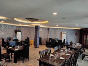 A restaurant with multiple dining tables and chairs, patterned wallpaper, and ceiling lights.