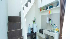 A compact kitchen with a staircase, a small dining area, and a window with curtains. - Cozzy Villa Azzalia (batu)
