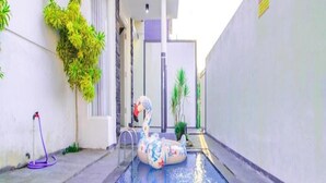 A swimming pool with a floating toy, surrounded by walls and potted plants. - Cozzy Villa Azzalia (batu)