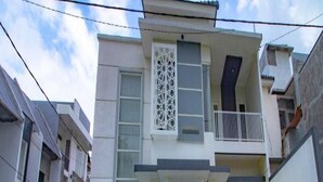 A two-story residential building with a balcony, a gated entrance, and a parked motorcycle. - Cozzy Villa Azzalia (batu)