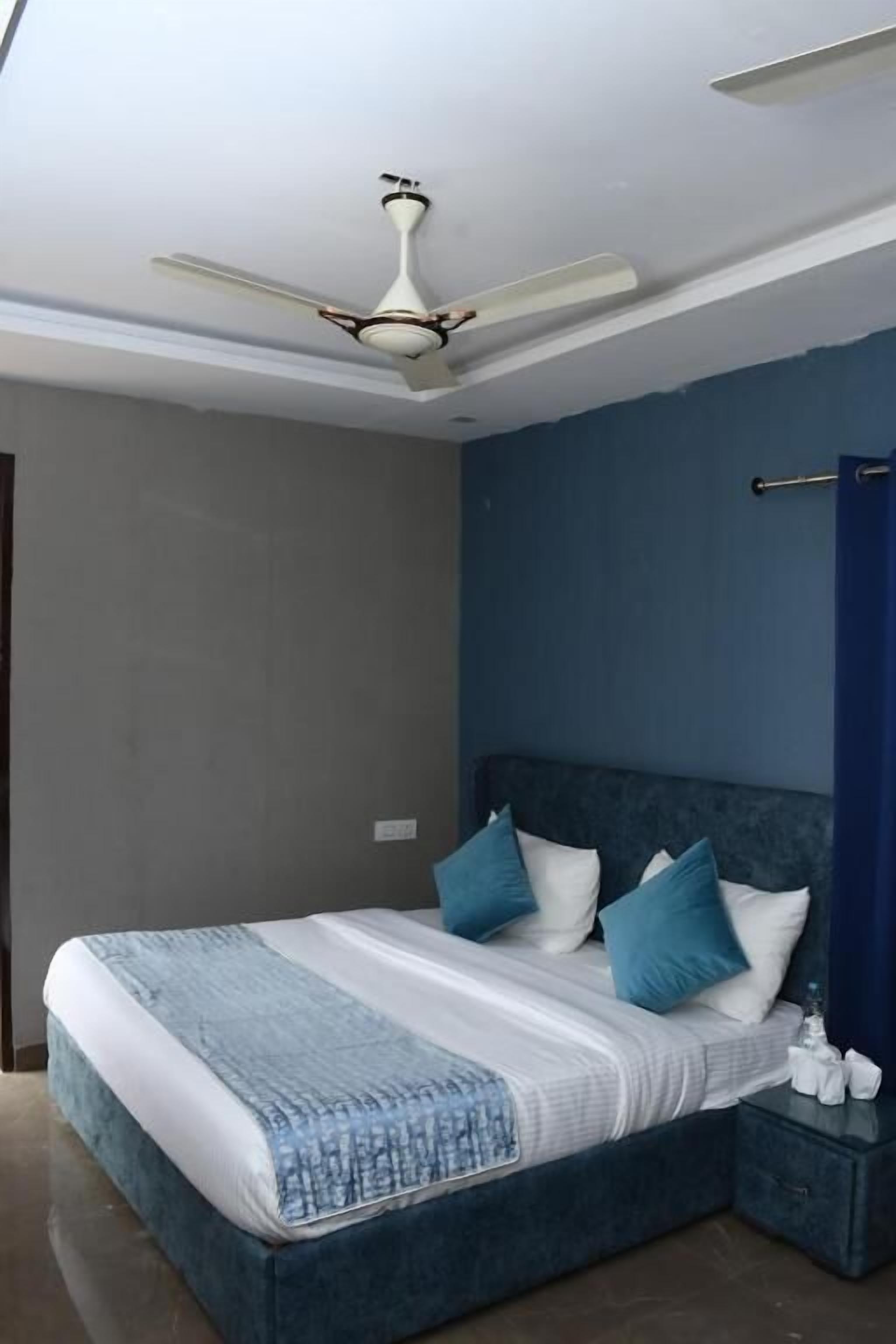 Quarto com cama, mesa de cabeceira, ventoinha no teto e luminária.
