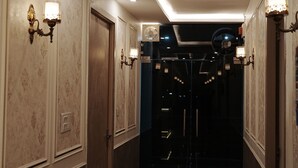 A hallway with wall-mounted sconces, a ceiling fan, and a door leading to a darker room. - VENUS INN ROOMS  AND BANQUETS (Lucknow)