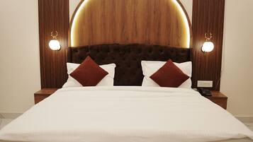 A large bed with a tufted headboard, two bedside tables with lamps, and a wall-mounted light fixture.