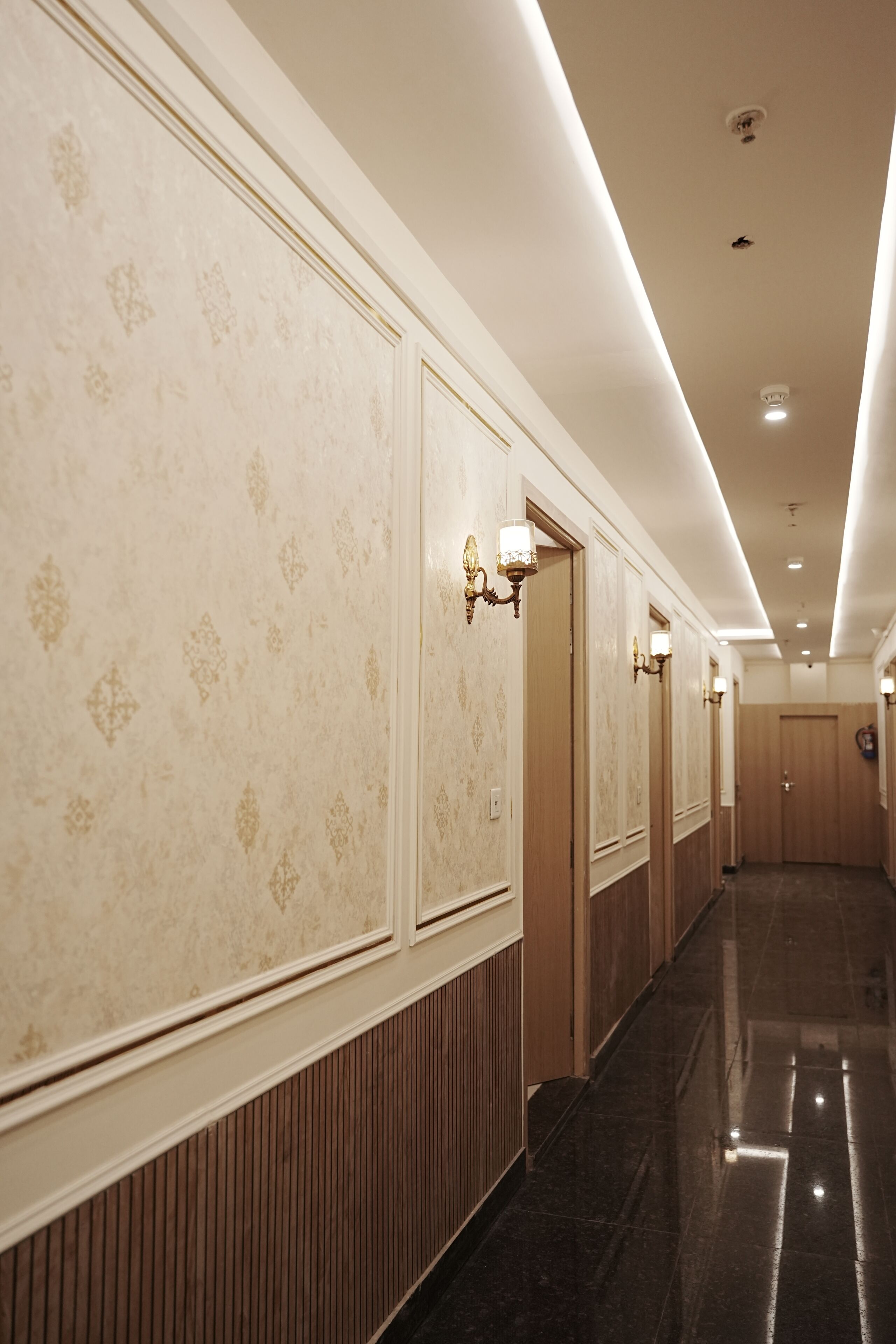 Un pasillo de hotel con papel tapiz estampado, paneles de madera y apliques en la pared.