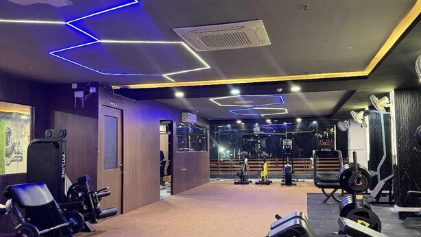 A gym with exercise equipment, a mirror, and a wall-mounted fan. - VENUS INN ROOMS  AND BANQUETS (Lucknow)