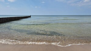 Ein Strand mit klarem Wasser, einer Holzstege und einem sandigen Ufer.