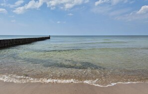 A beach with clear water, a wooden pier, and a sandy shore. - Nice home in Darlowo with sauna (Darlowo)
