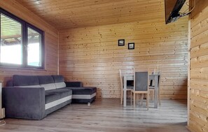 A cabin interior with a sofa, a dining table with chairs, and wooden walls. - Nice home in Darlowo with sauna (Darlowo)