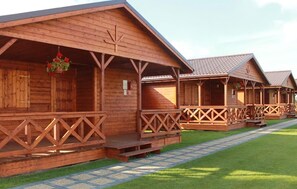 A row of wooden cabins with balconies, arranged on a paved path with grass. - Nice home in Darlowo with sauna (Darlowo)