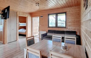 A wooden cabin interior with a dining table, chairs, a sofa, and a television. - Nice home in Darlowo with sauna (Darlowo)