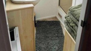 Un bagno piccolo con un lavandino, una finestra ornata da una tenda a farfalle e un tappeto scuro.