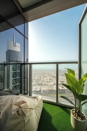 Quarto de hotel moderno em um arranha-céu, com uma grande janela e vista para a cidade, cama com piso de grama artificial verde e planta em vaso.