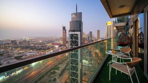Um edifício alto com varanda de vidro, com vista para o horizonte urbano ao entardecer.