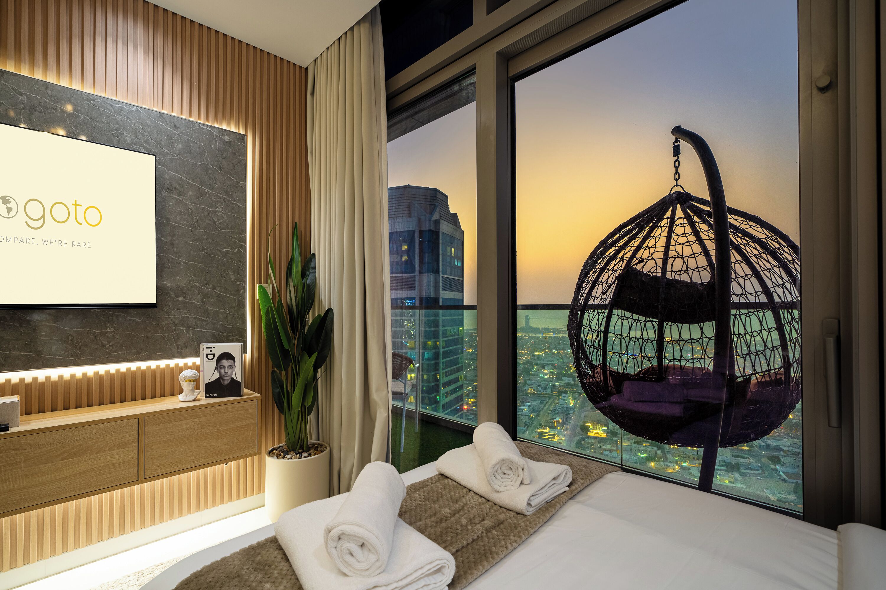 Hotelkamer met een bed, een hangstoel, uitzicht op de stad en een receptiebalie.