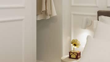 Un dormitorio con una cama, una mesita de noche con un gramófono y un armario con ropa colgada.